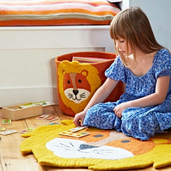 A little girl sitting on the floor with a Felt Handmade Kids Lion Rug and Storage Basket.