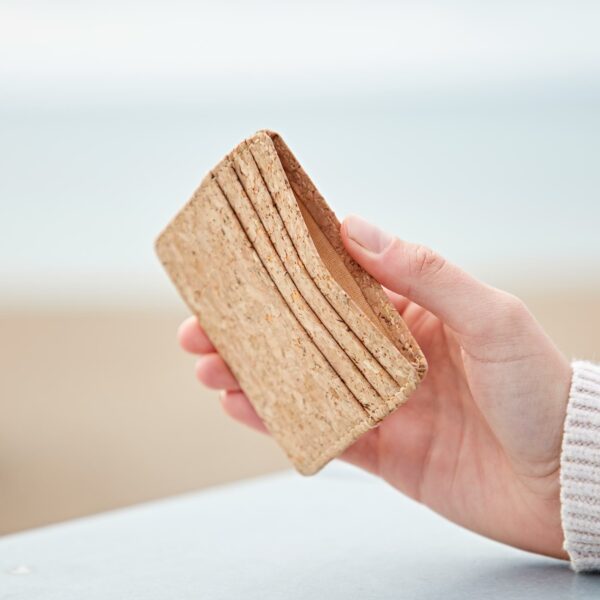 A person holding up a Natural Cork Credit Card Holder on the beach.