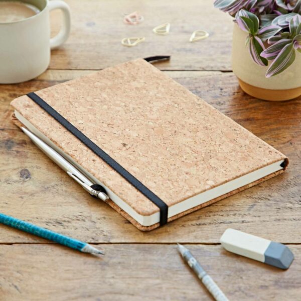 A personalised Natural Cork A5 Notebook on a wooden table with pens, pencils and a cup of coffee.