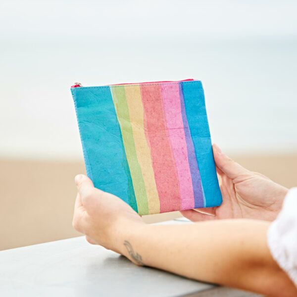 A woman holding up the Recycled Plastic Rainbow Pouch on the beach.