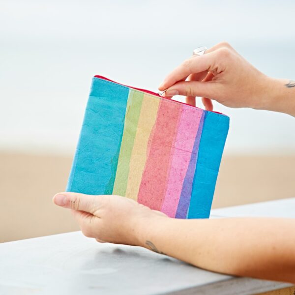 A woman holding a Recycled Plastic Rainbow Pouch on the beach.