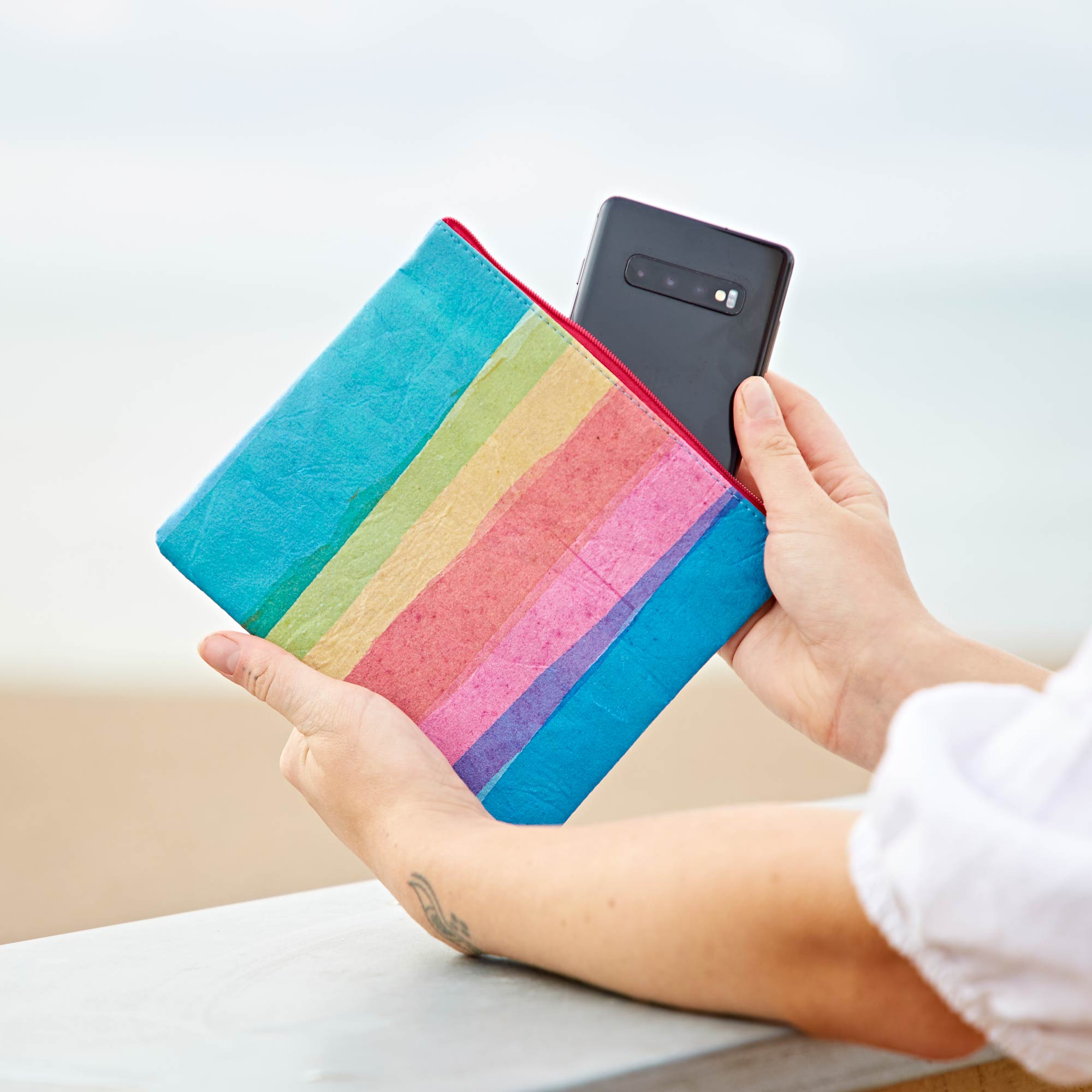 A woman holding up a Recycled Plastic Rainbow Pouch made from recycled plastic.