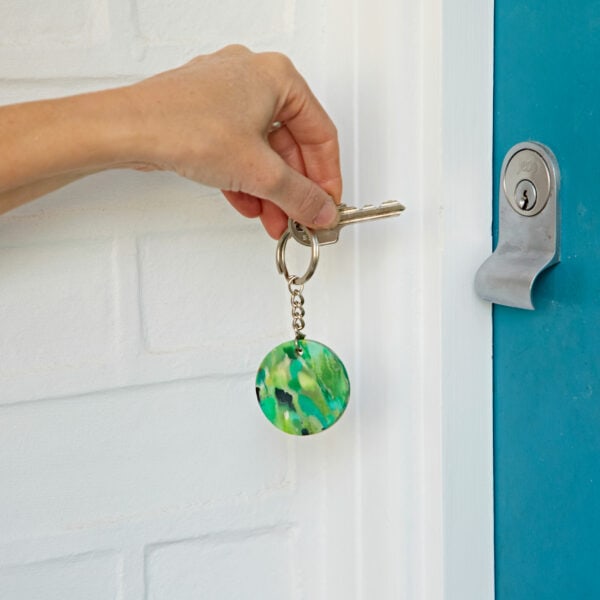 A person opening a blue door with a green ball keychain made of recycled plastic.