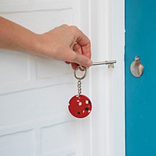 A person opening a door with a red keychain made from recycled plastic.