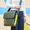 A woman wearing jeans and a green Recycled Plastic and Seat Belt Messenger Bag made from recycled plastic.