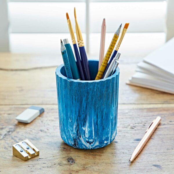 A blue pencil holder made from recycled plastic on a table with pens and pencils.