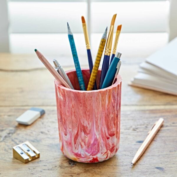 A multicoloured vase filled with pens and pencils on a table.