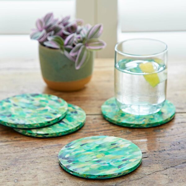 Four recycled coasters made from plastic on a table next to a glass of water.