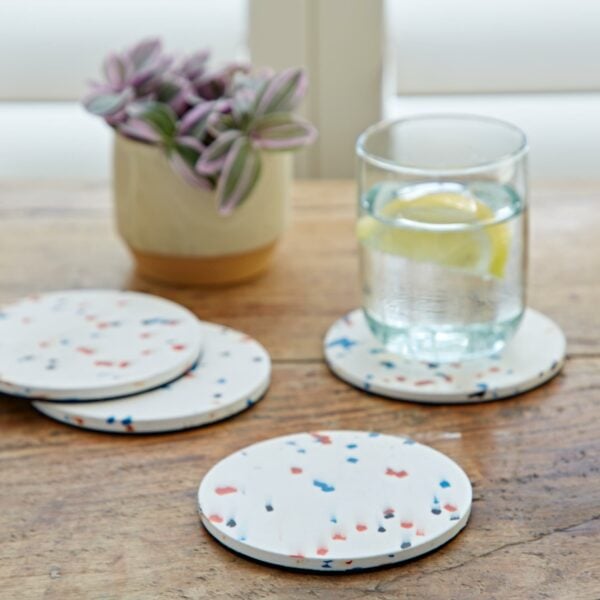 Four round confetti coasters made of recycled plastic on a wooden table.