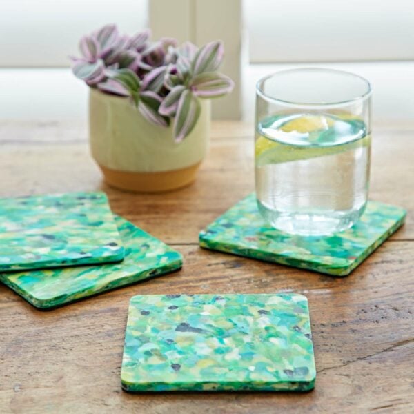 Four green plastic coasters on a table next to a glass of water.