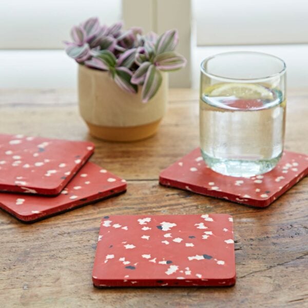 A set of red and white confetti coasters on a wooden table made from recycled plastic.