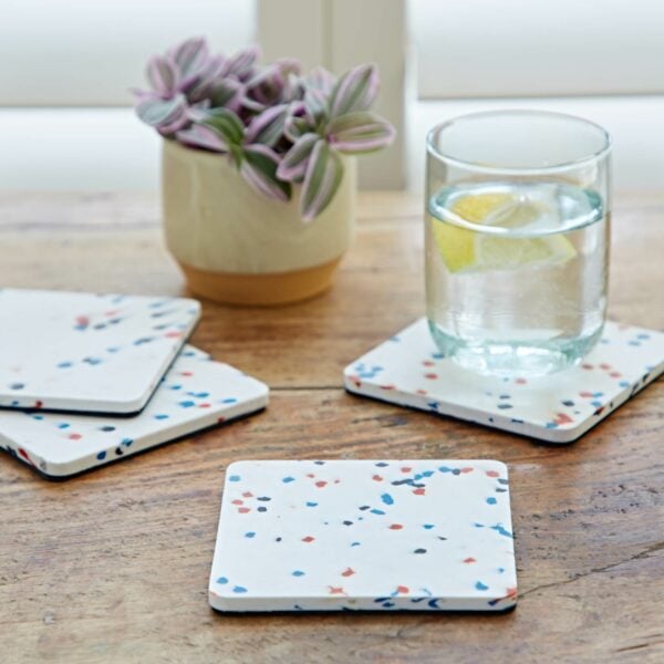 Four square plastic coasters made from recycled materials on a wooden table.