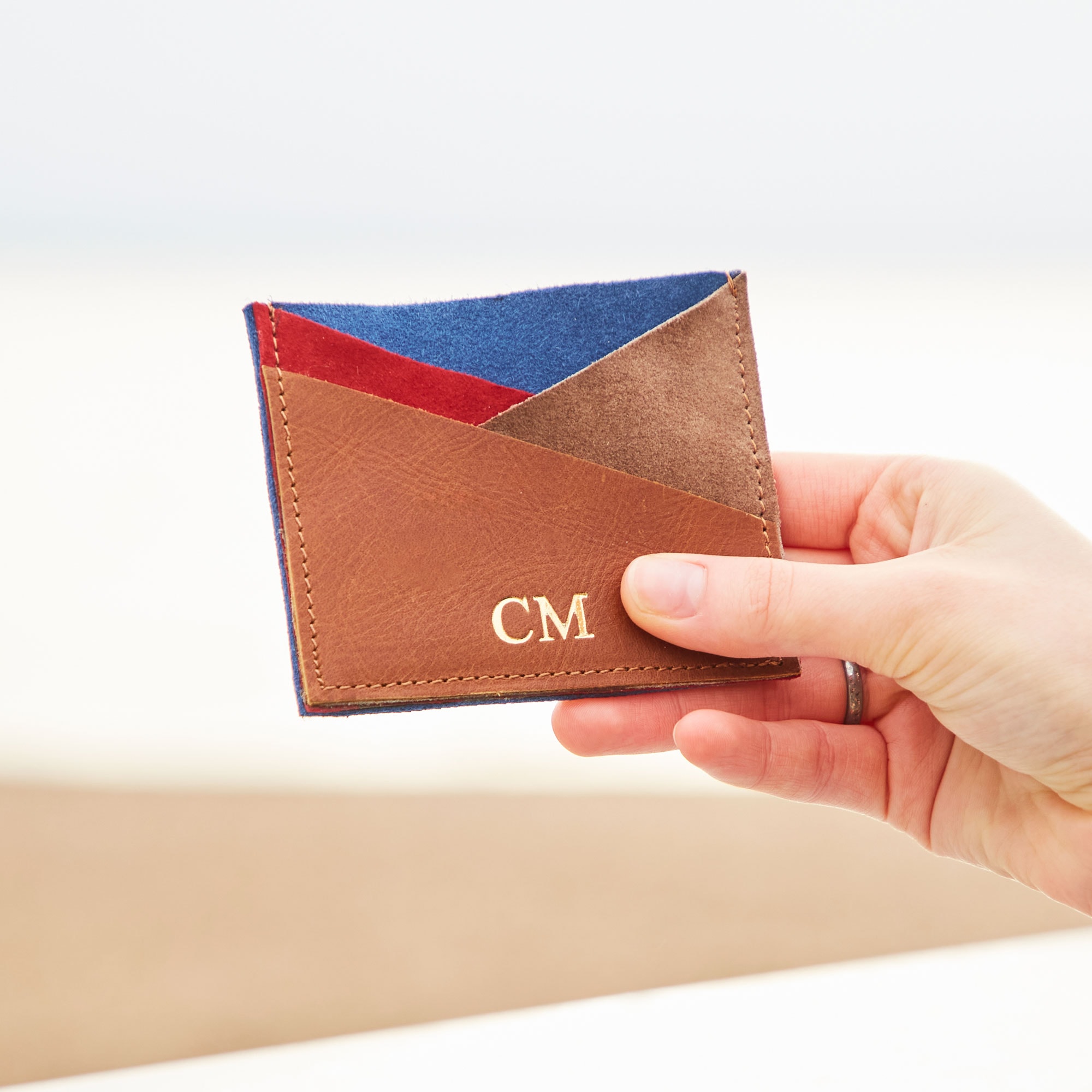 A person holding up a Leather and Suede Credit Card Holder with a monogram on it.