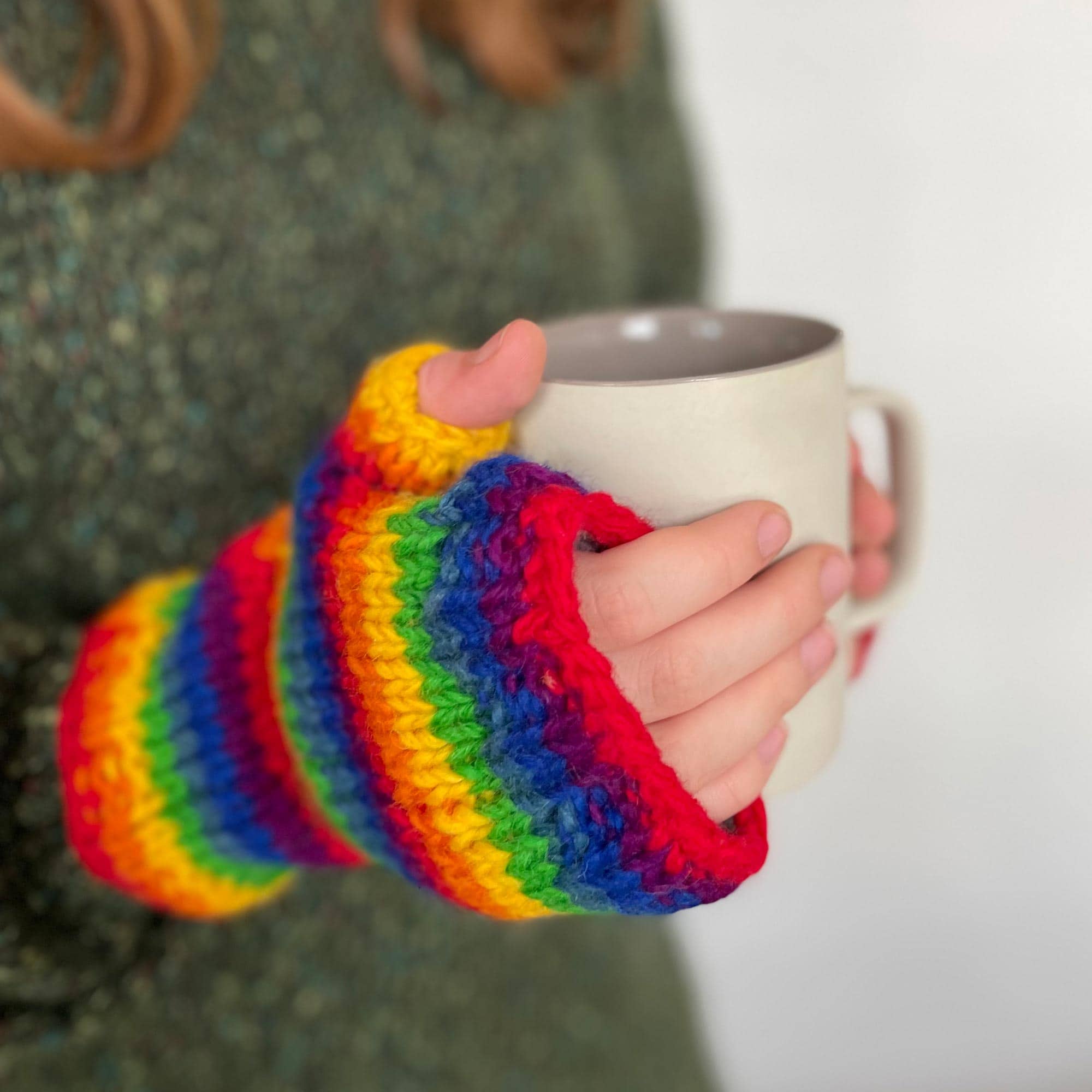 A woman is holding a cup of coffee and a pair of Woollen Fairisle Handwarmer Gloves, perfect for keeping her hands warm in style.