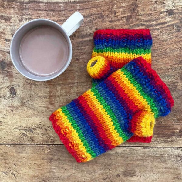 A pair of Woollen Rainbow Handwarmer Gloves next to a cup of coffee.