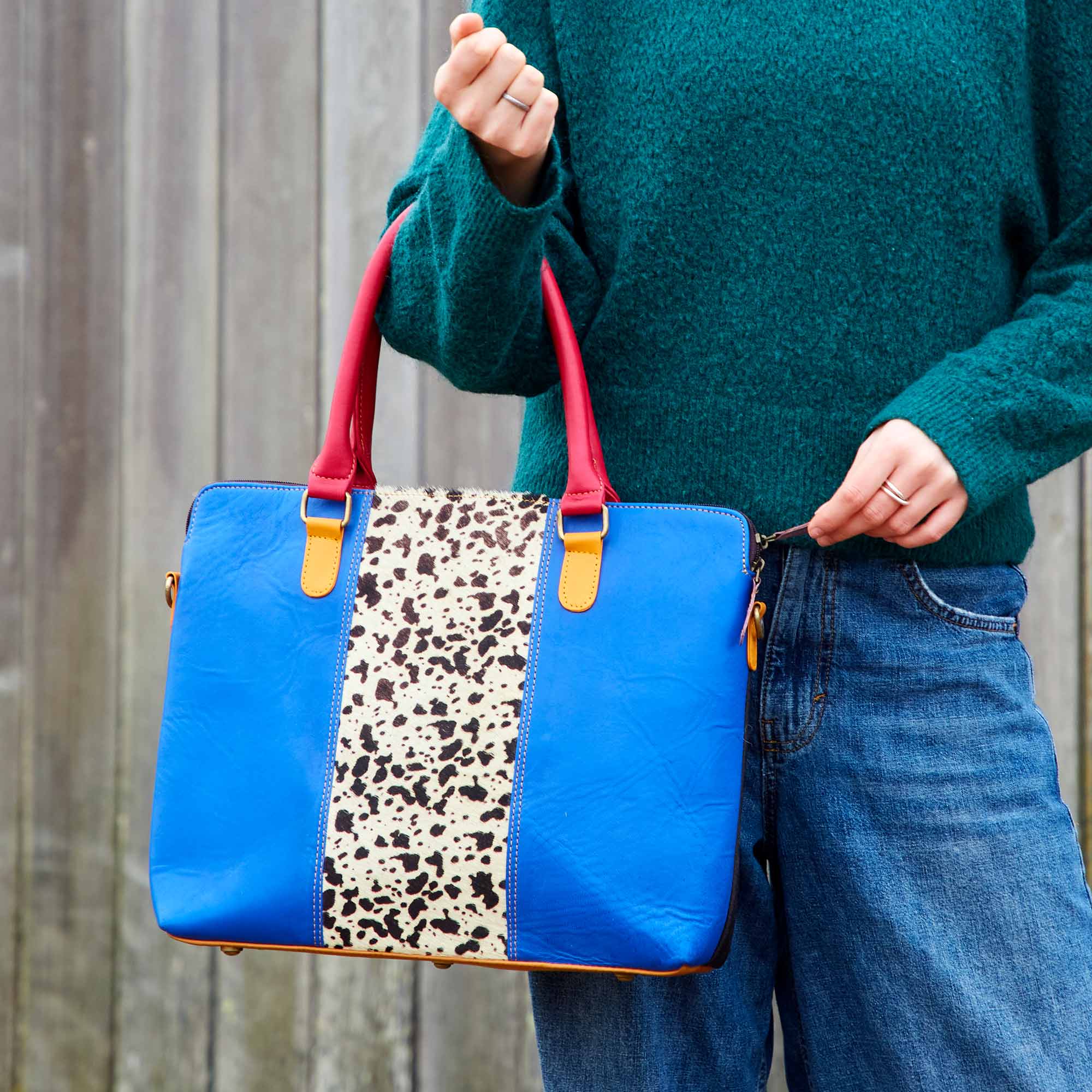 Kiara, a woman, holding a recycled leather handbag in blue and red leopard print.