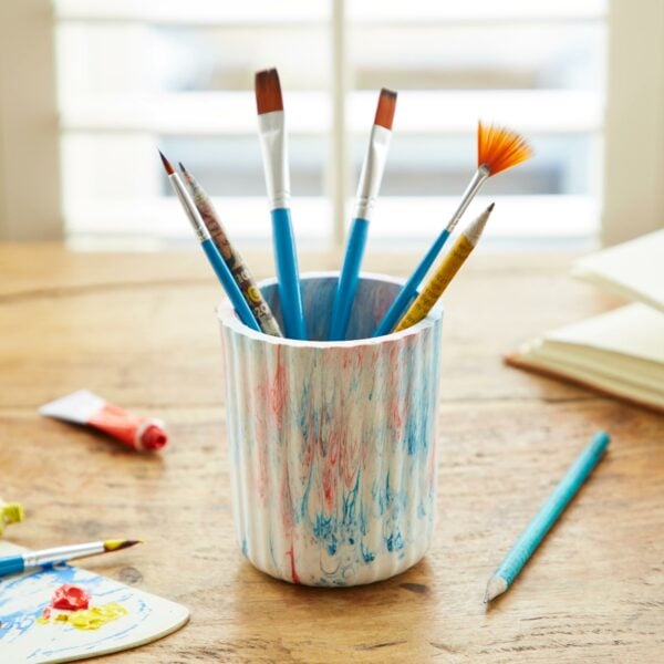 A tumbler of paint brushes on a wooden table.