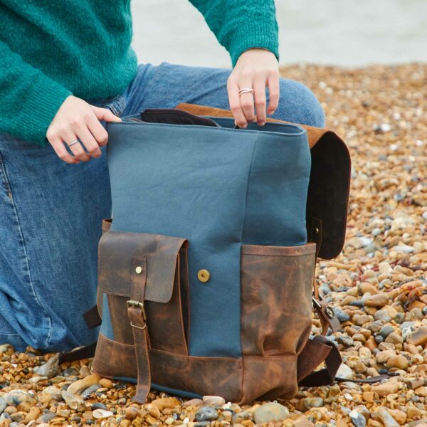 A woman is holding a Personalised Buffalo Leather And Blue Canvas Backpack on the beach.