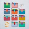 A grid of ten colorful wallets, featuring the Personalised Iman Recycled Leather Small Purse, two bus tickets, a credit card, and coins are arranged on a light surface.