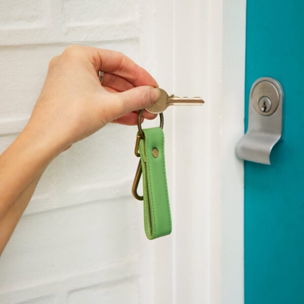 A person holding a recycled leather keyring with a key to a blue door.