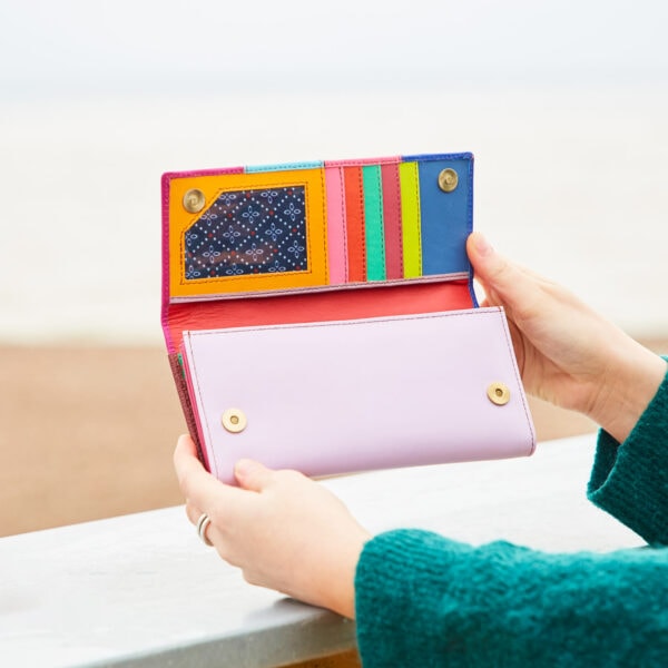 A woman holding a Meena Recycled Leather Multicoloured Stripe Clutch Purse on a beach.