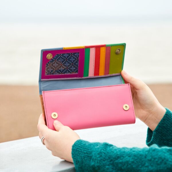 A woman holding a Personalised Meena Recycled Leather Multi-Coloured Stripe Clutch Purse on a beach.