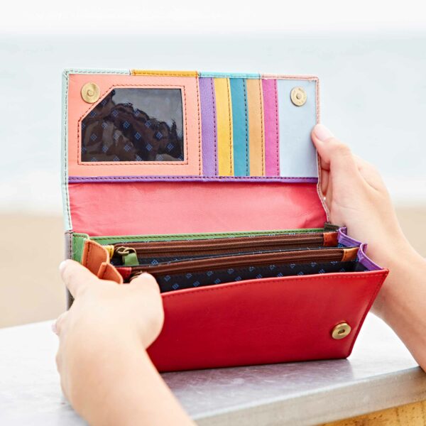 A woman's hand holding a Meena Recycled Leather Multicoloured Stripe clutch purse on a beach.