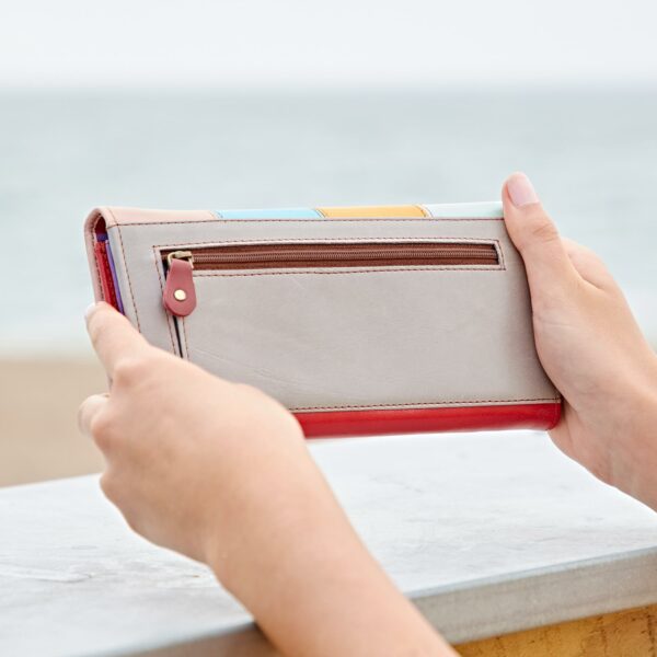 A person holding a Meena Recycled Leather Multicoloured Stripe Clutch Purse on the beach.
