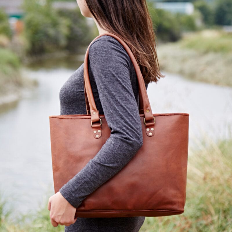 A woman holding a brown leather tote bag.