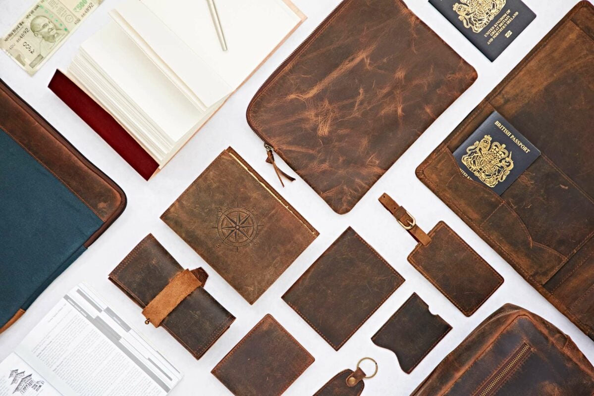 A flat lay of brown leather travel bags and accessories, featuring wallets, a notebook, a passport holder, a keychain, and a pencil case, all arranged neatly on a white surface.