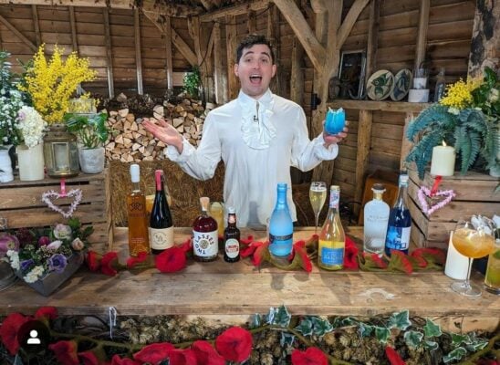 A man standing in front of a table with a lot of bottles, and our red felt flower garland.