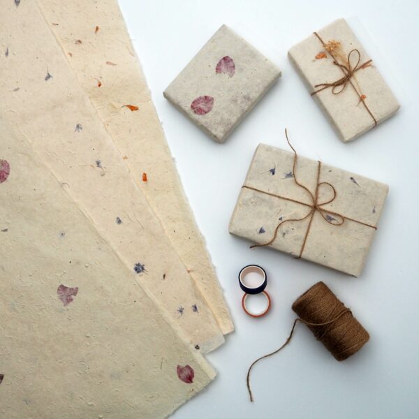 Petaled Natural Lokta Gift Wrap showcasing paper sheets with petals, three gifts wrapped and tied with twine, a spool of twine, and two small containers on a white surface.