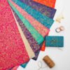 The Paisley Lokta Gift Wrap, featuring vibrant gold paisley patterns, is spread out. Nearby are brown twine, dried flowers, and rolls of tape—the perfect set for creative gift wrap projects.