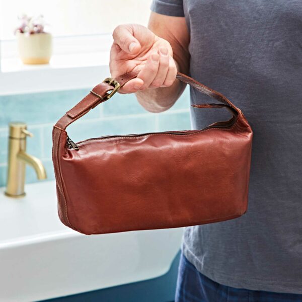 A person holding a Personalised Brown Leather Wash Bag with Strap.