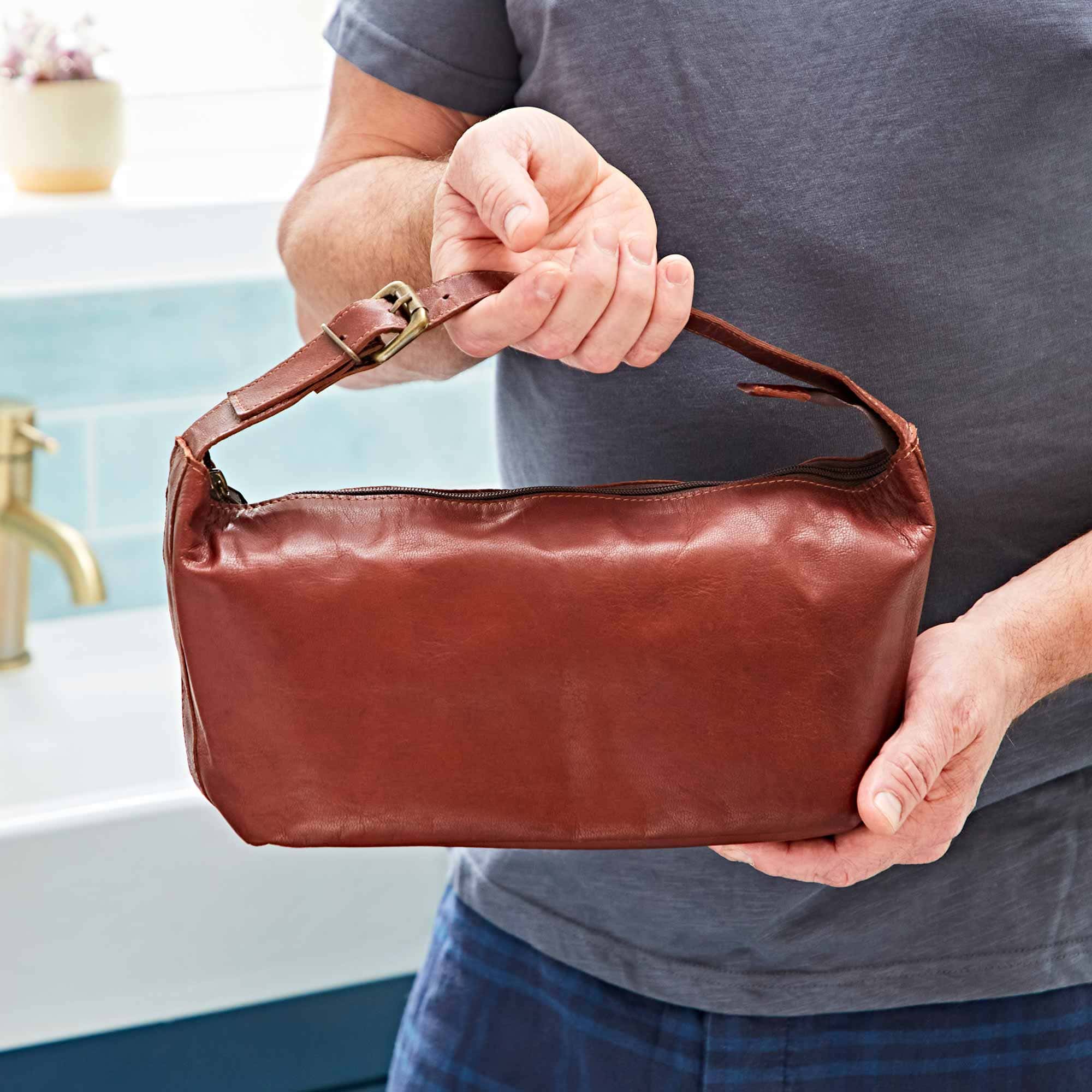 A man holding a Personalised Brown Leather Wash Bag with Strap.