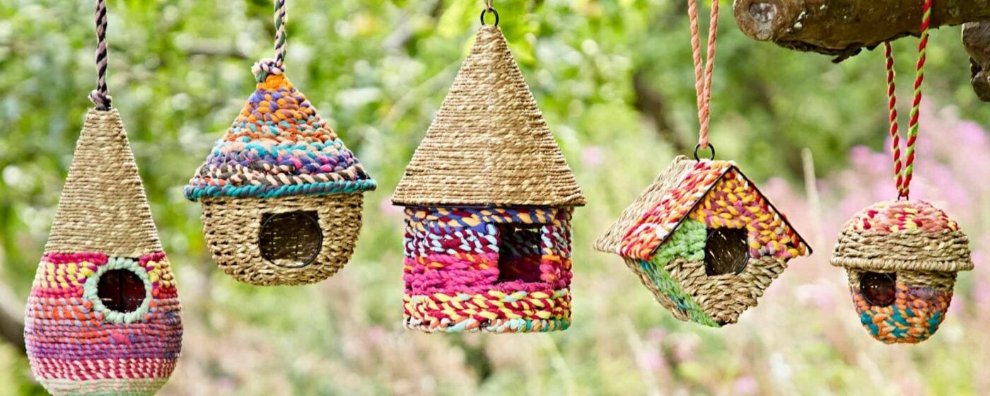 Colorful woven birdhouses hanging from a tree branch, perfect as a Mother's Day gift in a garden setting.