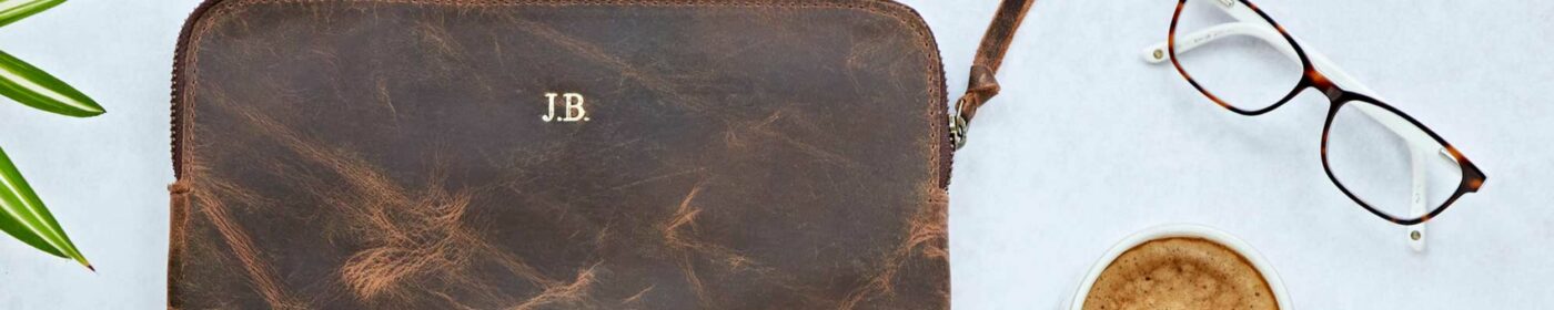 Leather pouch with initials "j.b." next to a pair of glasses and a Mother's Day gift cup of coffee on a white background.