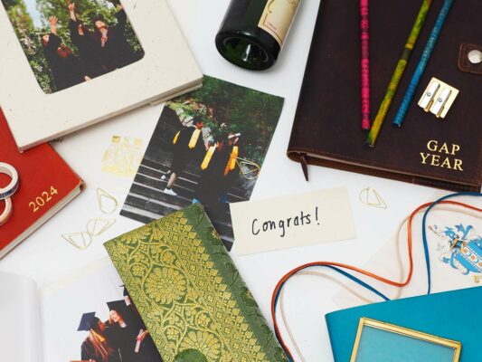 A collection of graduation items, including a "Congrats!" card, graduation photos, notebooks, and pens spread out on a surface. Find the perfect addition to your Fair Trade Father's Day gift guide amongst these treasures.