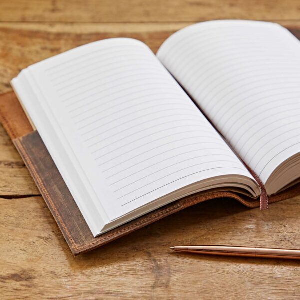 An open, Personalised Buffalo Leather Refillable Journal crafted from luxurious buffalo leather with lined pages rests on a wooden surface, accompanied by a gold pen lying beside it.