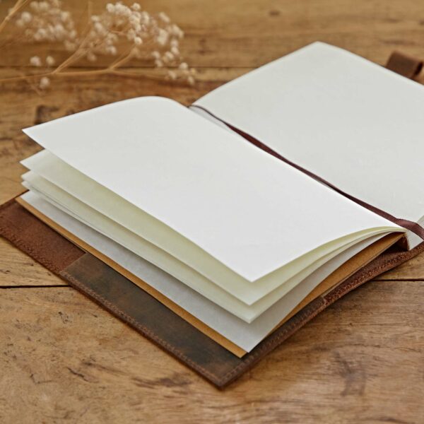 Open blank Personalised Buffalo Leather Refillable Tree of Life Journal with off-white pages and a brown buffalo leather cover, placed on a wooden surface with dried flowers in the background.