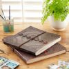 Two Indra Chakra Embossed Leather Albums with Semi-Precious Stones are placed on a wooden table next to a paint palette, paintbrushes in a jar, and a potted fern.