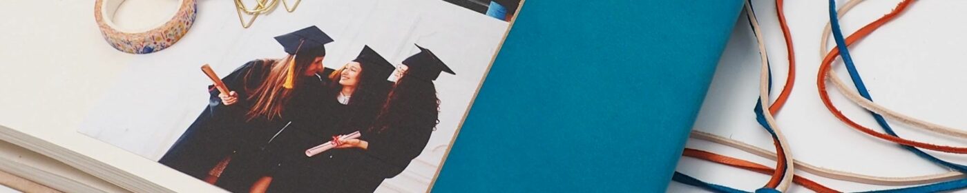 Three individuals in graduation caps and gowns celebrate in a photograph next to a blue notebook and colorful ribbons, perfect for inclusion in any Fair Trade Father's Day Gift Guide.