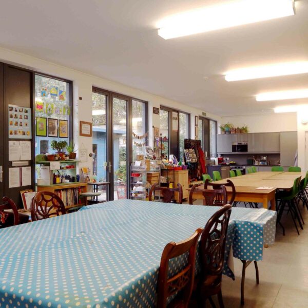 A room adorned with tables draped in polka dot tablecloths, wooden chairs, art supplies, shelves brimming with decorations, and a quaint kitchenette area in the background evokes the charming ambiance of a River Stour Wild Beaver Canoe Tour and Talk.