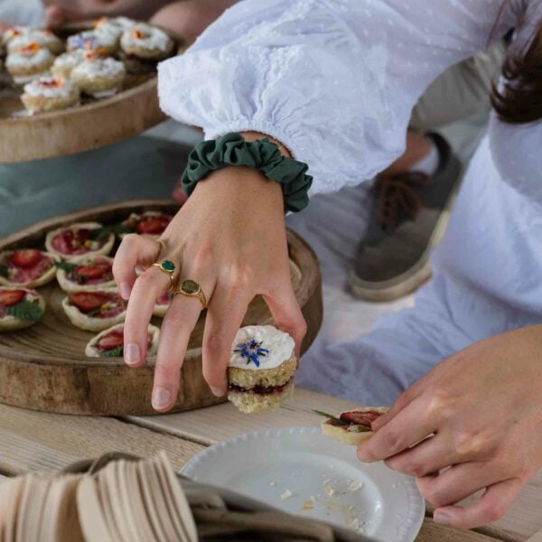 A person holding a small, decorated dessert in their left hand and meticulously preparing another with their right hand, displaying the same careful precision found in Hiver's Ultimate Beekeeping, Beer and Wine Tasting Experience for Two. A table with more similar desserts in wooden trays is visible.