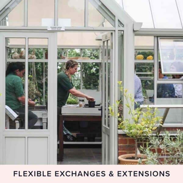 A person in a green shirt working at a table inside a greenhouse, visible through open doors, with plants surrounding the workspace. Text below reads "FLEXIBLE EXCHANGES & EXTENSIONS." This scene could be straight out of the Half Day The Edible Garden Course at The Raymond Blanc Gardening School, Le Manoir aux Quat Saisons.