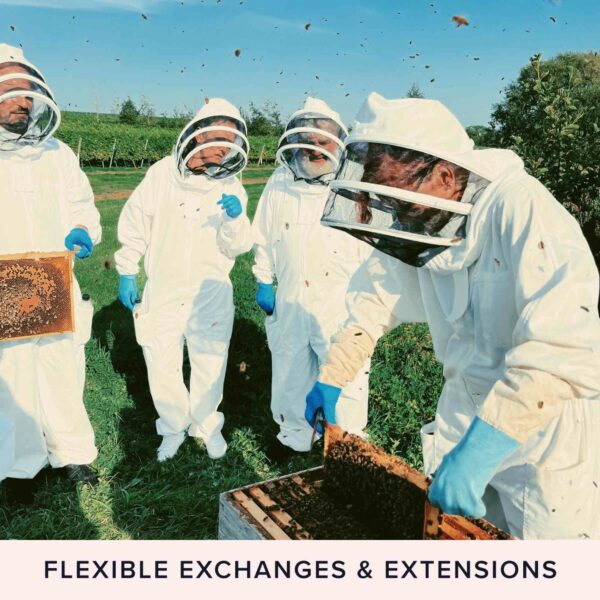 Four people in beekeeper suits are inspecting a hive outdoors. All are wearing white suits, blue gloves, and protective headgear. Bees are visibly flying around. The text reads "FLEXIBLE EXCHANGES & EXTENSIONS." Dive into the Hiver's London Beekeeping and Beer Tasting Experience for Two and get a taste of nature's buzz!