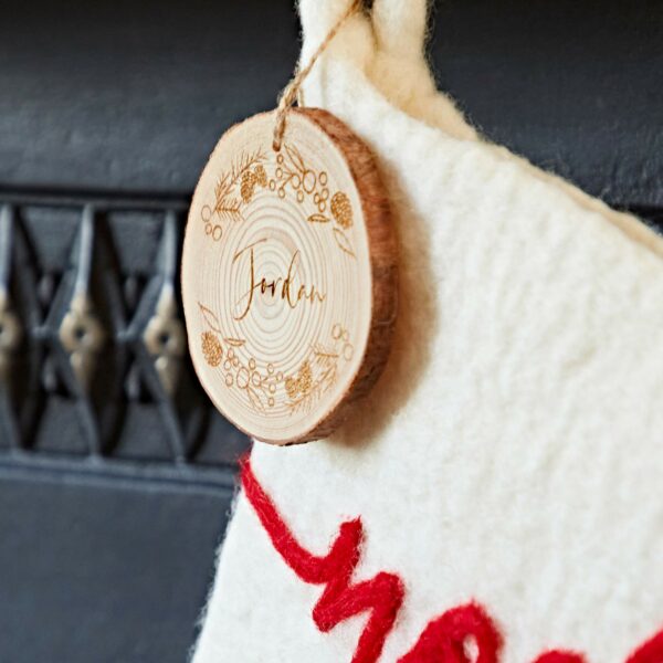 A festive Felt Christmas Stocking in white and red holds a wooden ornament engraved with the name "Jordan.