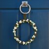A Felt Mistletoe Christmas Wreath, adorned with green leaves and felt mistletoe berries, hangs on a blue door with a silver door knocker.