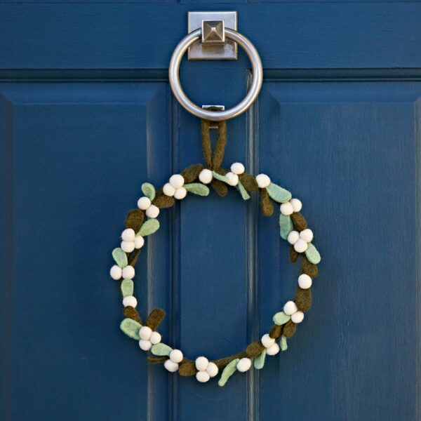 A Felt Mistletoe Christmas Wreath, adorned with green leaves and felt mistletoe berries, hangs on a blue door with a silver door knocker.