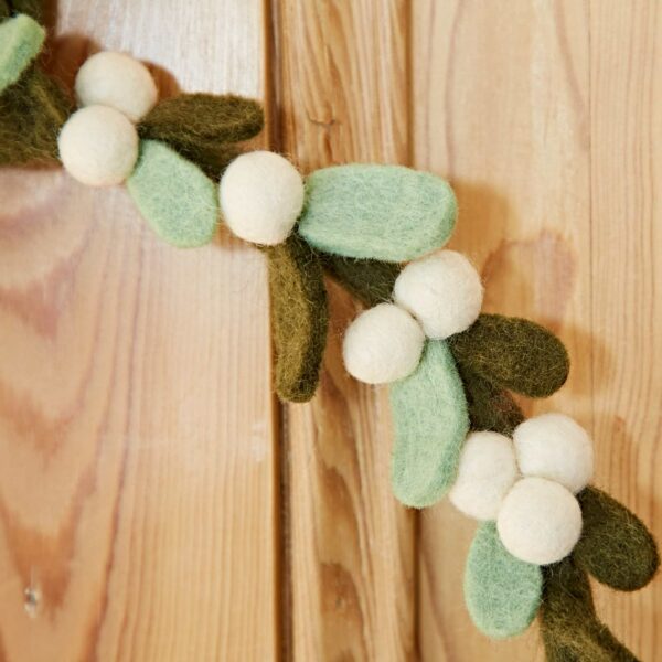 The "Felt Greenery with Pompoms Christmas Wreath," featuring green and white felt balls, hangs elegantly against a wooden background.